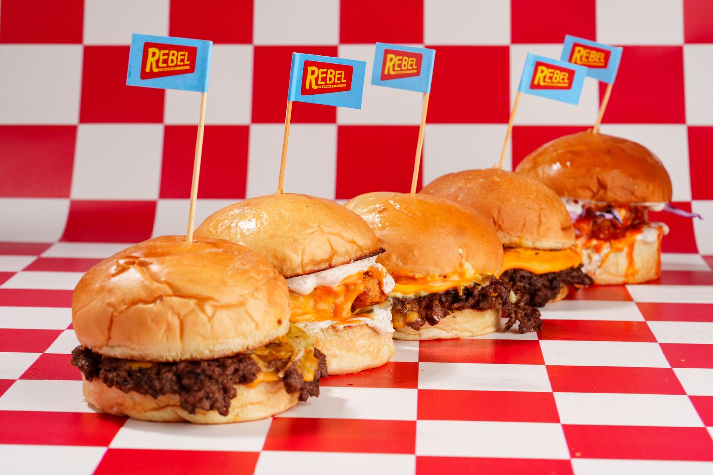 Damalı zemin üzerinde sıralanmış beş smash burger, üzerlerinde Rebel bayrakları